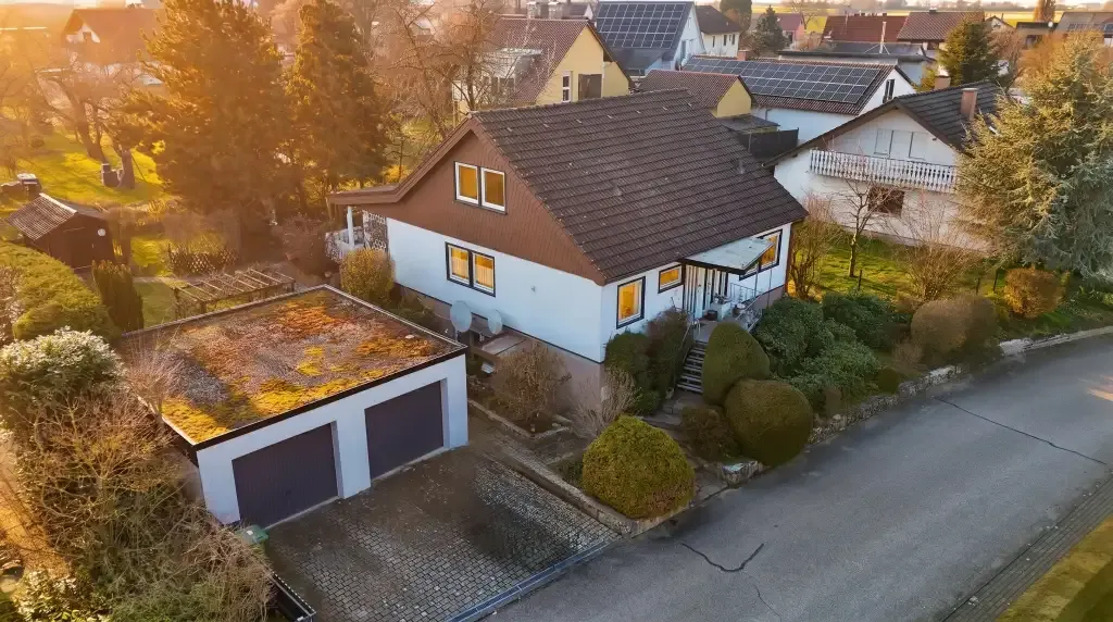 Luftaufnahme eines freistehenden Einfamilienhauses mit Doppelgarage und Garten in einem Wohngebiet bei Sonnenaufgang.