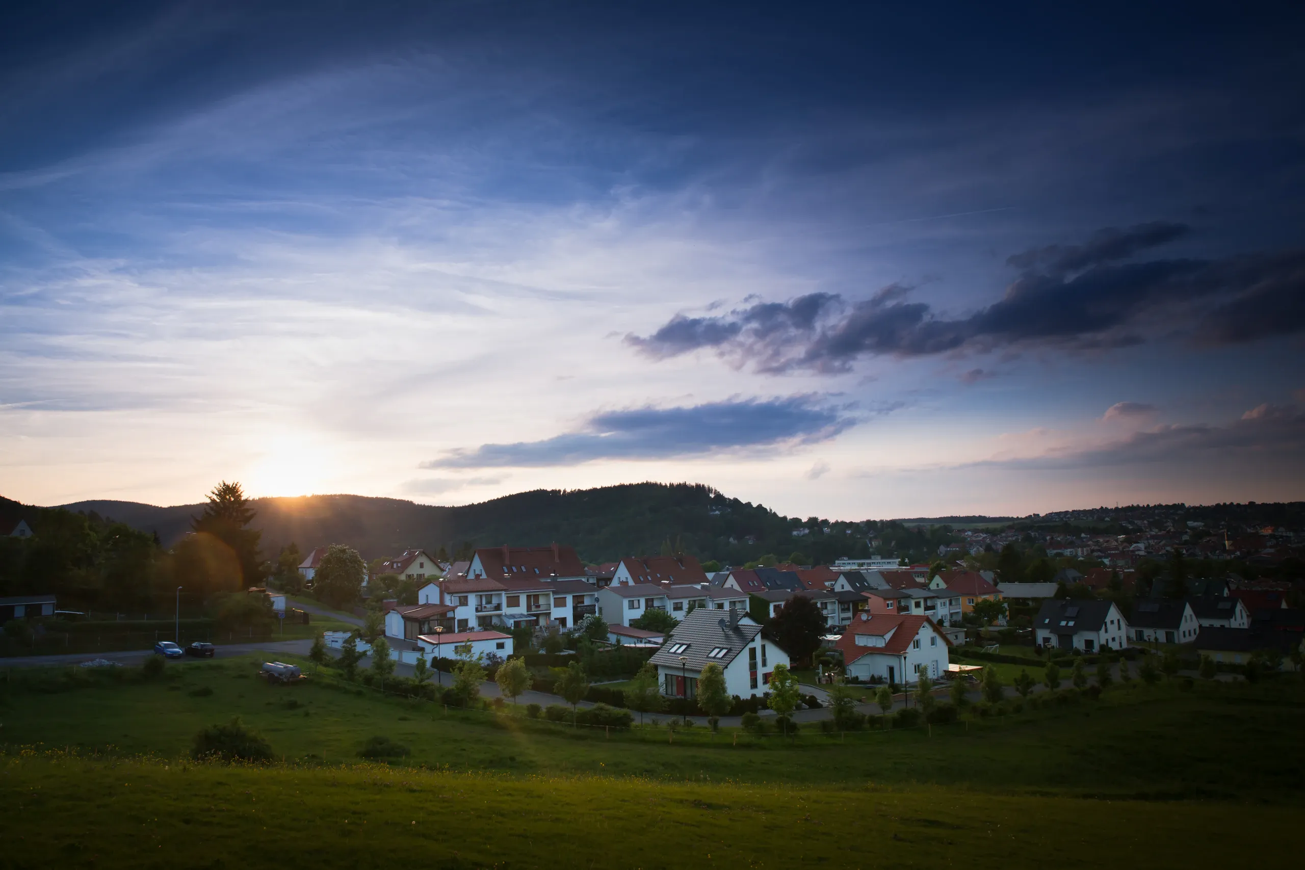 Wohnsiedlung mit Einfamilienhäusern vor Hügeln im Abendlicht.
