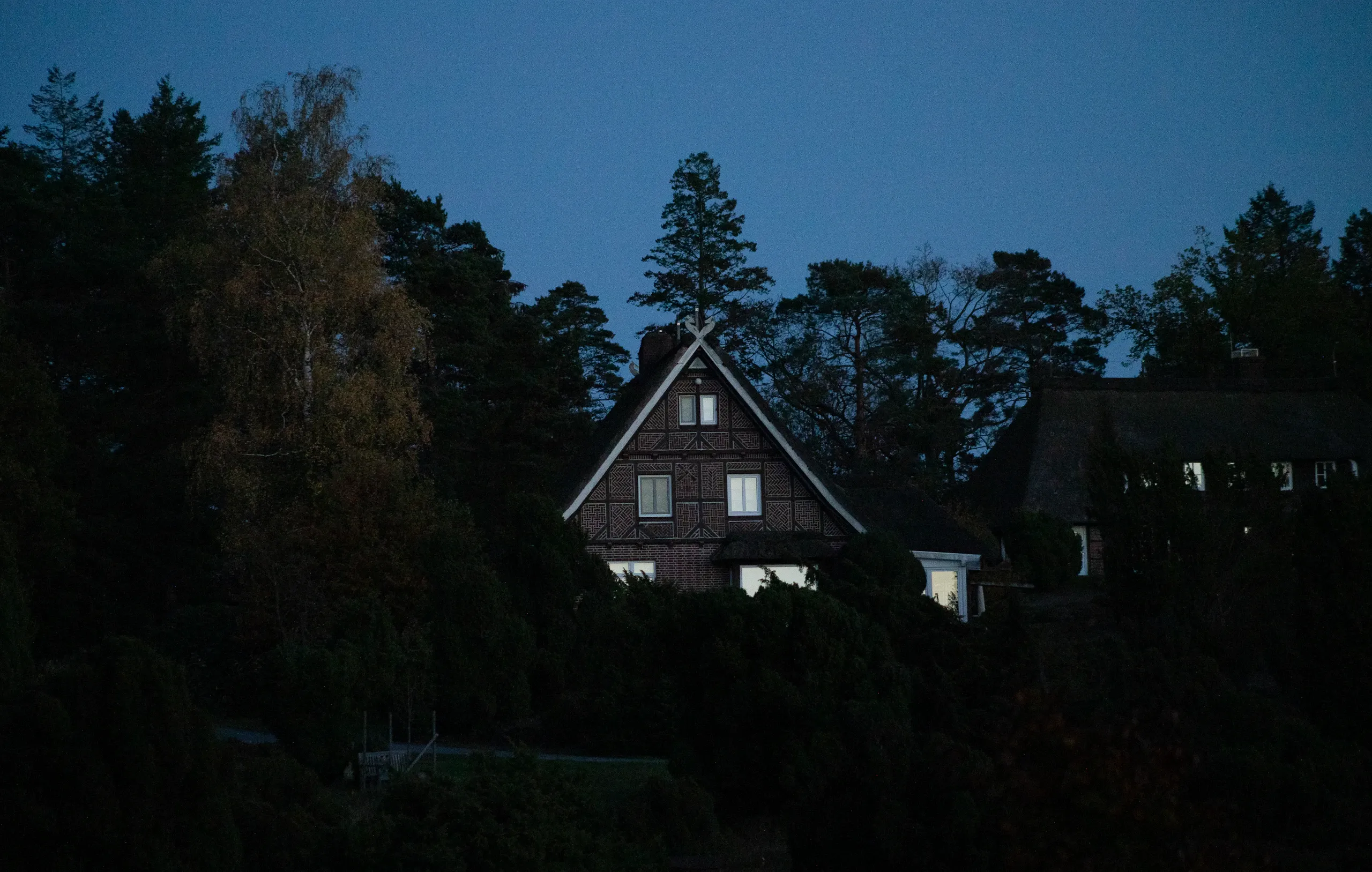 Einfamilienhaus mit warm erleuchteten Fenstern zwischen Bäumen in der Abenddämmerung.