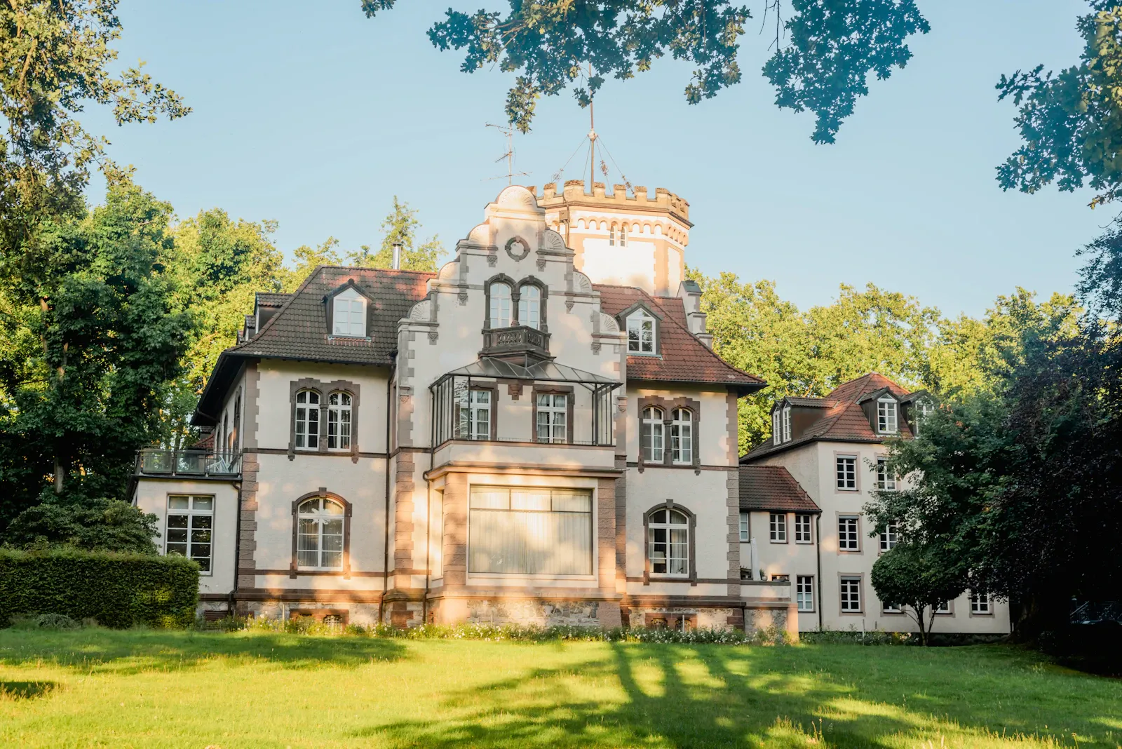 Ältere Villa mit Türmchen in einem sonnigen, gewachsenen Garten — Sinnbild für Immobilien aus Nachlässen.