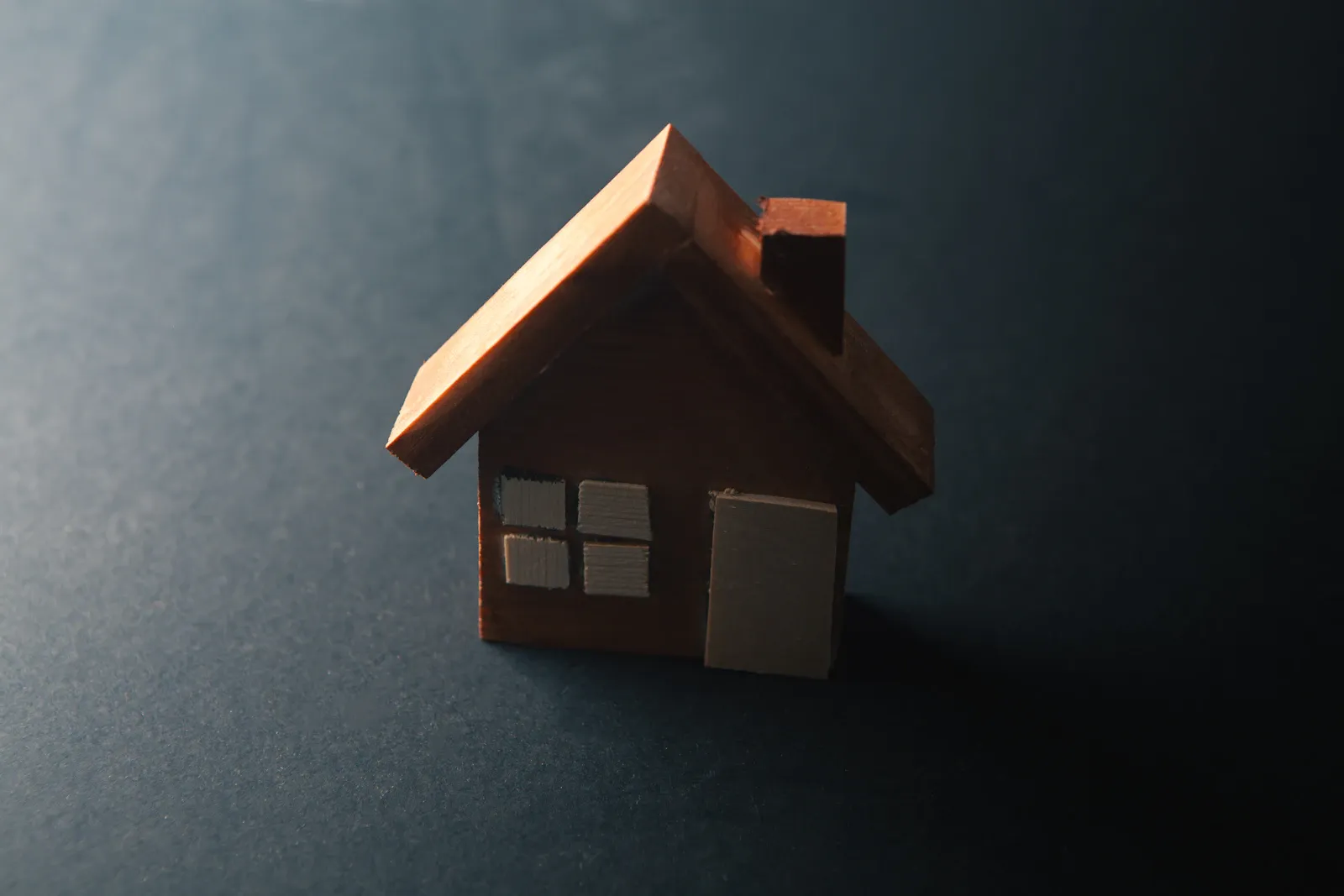 Kleines Holz-Hausmodell auf dunklem Untergrund — Sinnbild für die Immobilienbewertung.